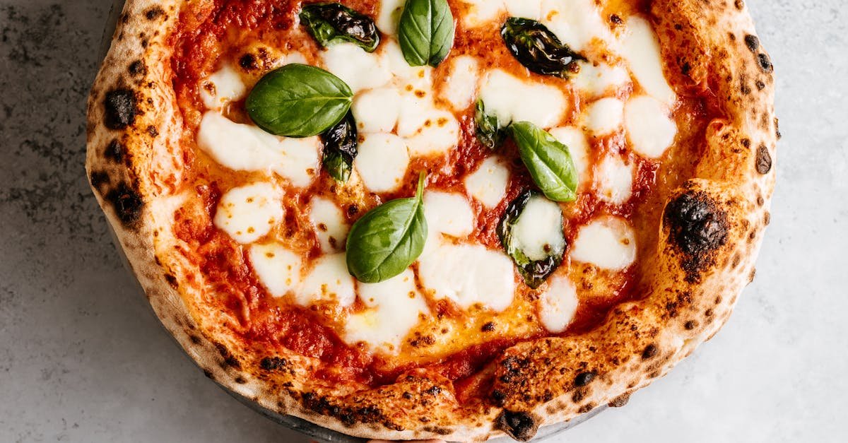 Close-up of a fresh Margherita pizza with mozzarella and basil, held over a gray background.